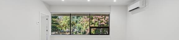 A spacious room with wooden flooring and a large window with a view of trees.