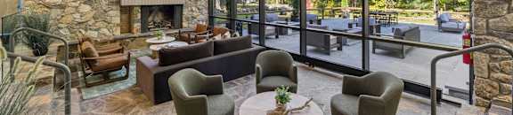 A modern living room with a stone fireplace and a glass wall overlooking the outdoors.