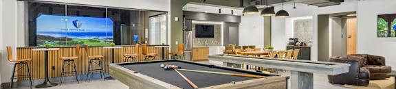 A pool table is in the middle of a room with a bar and a TV.