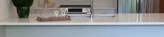 A kitchen with white cabinets and a counter with four stools.