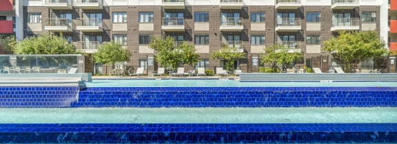 a large pool with a blue tile wall and an apartment building in the background