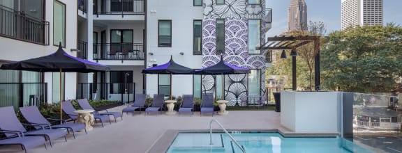 a swimming pool with chairs and umbrellas in front of an apartment building