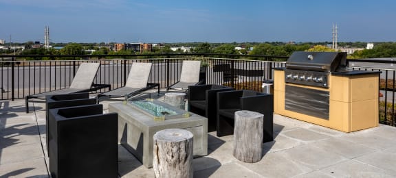 an outdoor terrace with a grill and lounge chairs with a view of the city in the