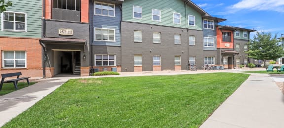 a sidewalk in front of an apartment building with a lawn at Switchback on Platte Apartments, Littleton, CO