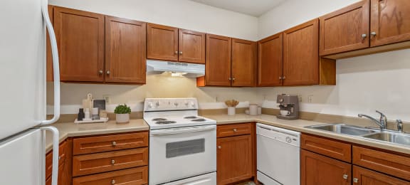 a kitchen with white appliances and wooden cabinets at Switchback on Platte Apartments, Colorado