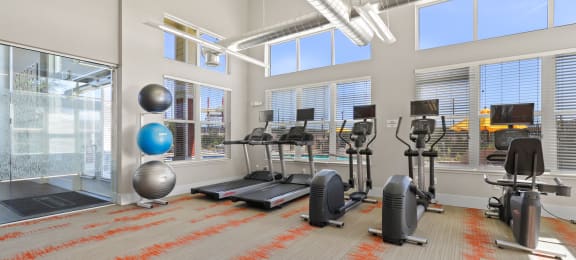 a gym with weights and exercise equipment in a building with large windows at Ridge at Thornton Station Apartments, Thornton, CO