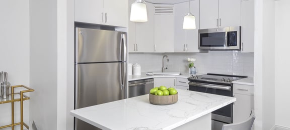 a white kitchen with stainless steel appliances and a marble counter top at River North Park Apartments, Chicago, 60654