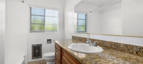 Apartments for Rent in Van Nuys CA - Colonial Manor - White Bathroom with Tub, Toilet, Granite Sandy Vanity, Mirror, and Tan Cabinetry