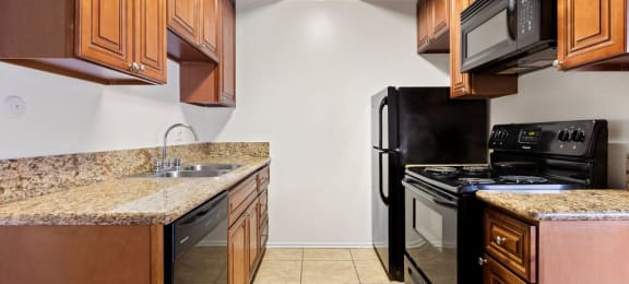 Canoga Park CA Luxury Apartments - Parthenia Terrace - Kitchen with Granite-Style Countertop, Brown Cabinets, and Black Appliances.