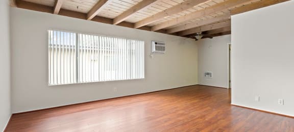 Canoga Park CA Luxury Apartments for Rent - Parthenia Terrace - Empty Living Room with Large Window, AC, Ceiling Fan, and Wood-Style Flooring.