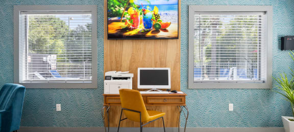 a computer desk with a yellow chair and a painting on the wall