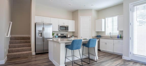 An open concept kitchen has an island with two stools in an apartment at Village Greens of Queen Creek