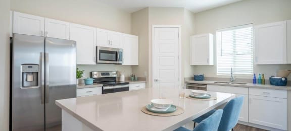 An island with 2 stools sits in the middle of a kitchen with stainless steel appliances at Village Greens of Queen Creek