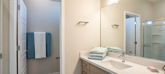 Model bathroom has a long mirrored vanity sink with storage in an apartment at Village Greens of Queen Creek