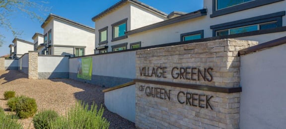 Landscaped wall along the property with a signat Village Greens of Queen Creek