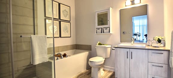 Spa like bathroom featuring standing, glass door shower and soaker tub at La Voile Broisbriand apartments