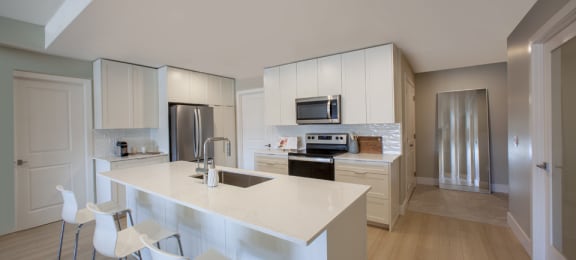 a kitchen with white cabinets and a white island with three white chairs
