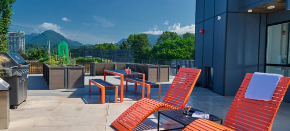 a rooftop deck with lounge chairs and a grill