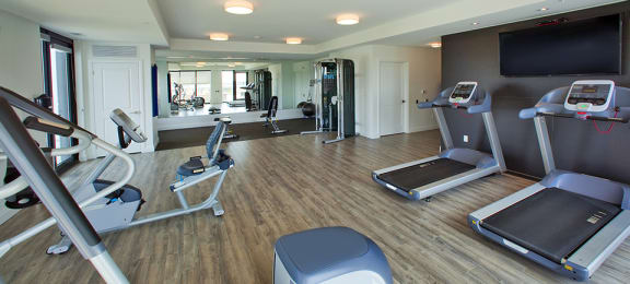 Fitness centre with cardio machines and free weight, yoga/stretching area seen in background at Trio on Belmont (Building B) in Kitchener, ON