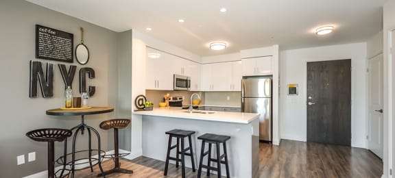 Two bars at a breakfast bar in an open-concept kitchen, with a dinette to the left, in a 1 bed 1 bath variation B in building A at Trio on Belmont in Kitchener, ON
