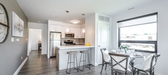 Dining area with table and chairs looking towards kitchen with bar stools at a breakfast bar Open-concept dining and living area looking towards patio door in a 2 bed + den 2 bath variation E in building A at Trio on Belmont in Kitchener, ON