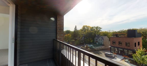 Private balcony with metal railing overlooking street and brick building across from it