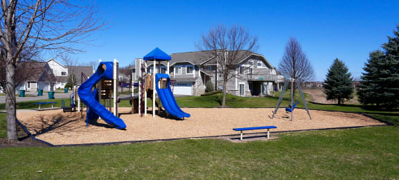 Community playground located on the property for time playing outside. Playground features two slides, a swing set, and multiple options of bench seating along the perimeter.