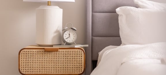 a nightstand with a lamp and a clock on it next to a bed