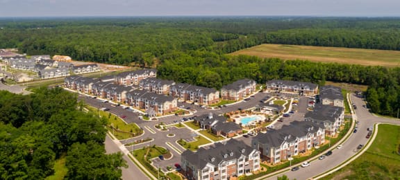 Overhead view of apartment buildings, clubhouse and pool; community is surrounded by trees and grass