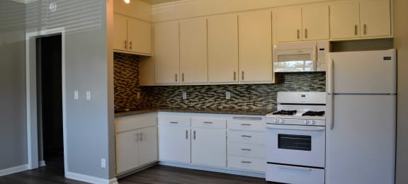 View of kitchen with wood look flooring, white cabinets, white appliances, and tile backsplash