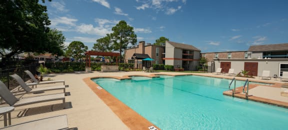 Gated community pool with lounge chairs, seating under umbrellas, and grilling station under pergola
