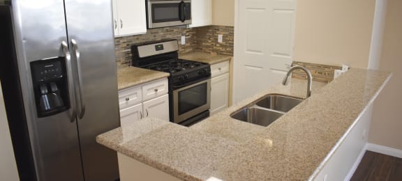 view of kitchen with stone counters, in laid sink, stainless appliances, and white cabinets