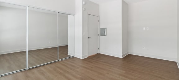 an empty room with white walls and wood flooring and a mirrored closet