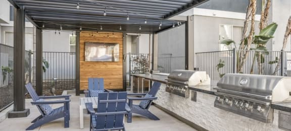 an outdoor patio with blue chairs and a grill and a tv