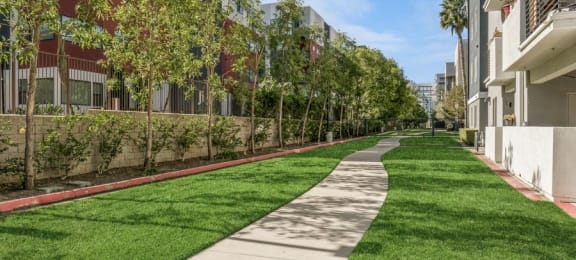 a walkway between two apartment buildings with green grass and trees