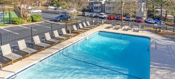 a swimming pool with chaise lounge chairs and a parking lot in the background