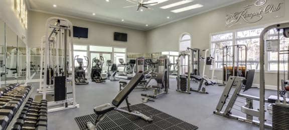 a spacious fitness center with cardio machines, free weights and strengthening machines. A mirrored wall with 2 tvs and ceiling fans.
