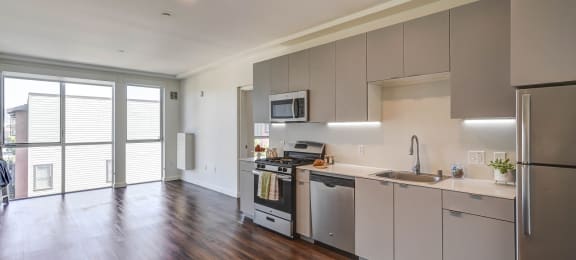 Contemporary kitchen featuring stainless-steel appliances, an open layout, sleek quartz countertops, and chic grey cabinets