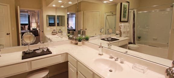 Luxury apartments with white cabinets, linen closet, extra cabinet space, cultured marble vanity, built-in vanity, roman tub with glass door and shower, and porcelain tiled floor at The Biltmore Apartments in Omaha, Nebraska