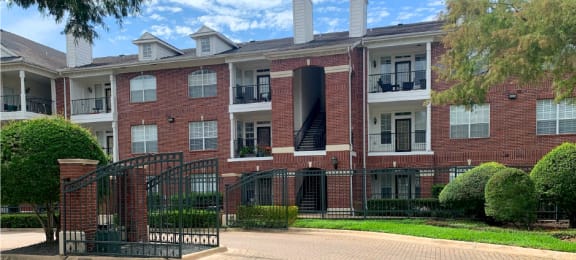 Gated community luxury apartments with brick exteriors, private outside storage, French doors, and lush landscaping including beautiful chaste trees at Tuscany Apartments in Houston.