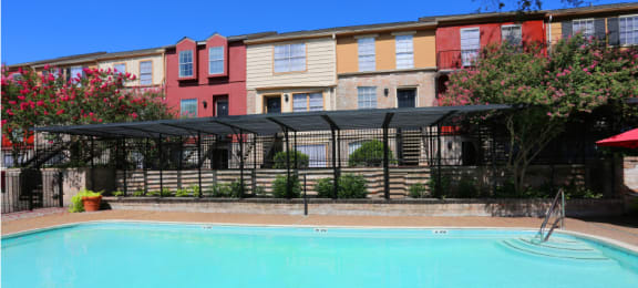 Large swimming pool with lush landscaping and colorful townhomes at Briarwood Apartments in Houston, Texas.