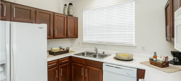 Spacious kitchen with honey brown toned cabinets with modern silver hardware, and white appliances including a double sided fridge with water and ice dispenser.