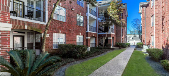 Luxury apartments with brick exteriors, beautiful landscaping, and patios with extra storage and French doors at Tuscany Apartments in Houston.