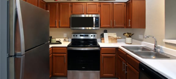 Luxury kitchen with wood plank floors, stainless steel appliances, honey brown cabinets, and white countertops at Lenox Village Apartments
