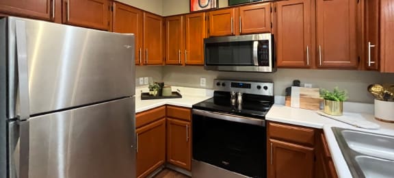 Luxury kitchen with wood plank floors, stainless steel appliances, honey brown cabinets, and white countertops at Lenox Village Apartments
