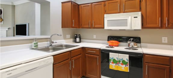 Luxury apartments with honey brown cabinets, tiled floors, white countertops, and u-shaped kitchen at Lenox Village Apartments in Lincoln, Nebraska