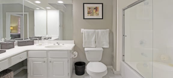 Spacious luxury bathroom with built-in cultured marble vanity, roman tub with glass shower, and porcelain tiled floor at The Biltmore Apartments in Omaha, Nebraska
