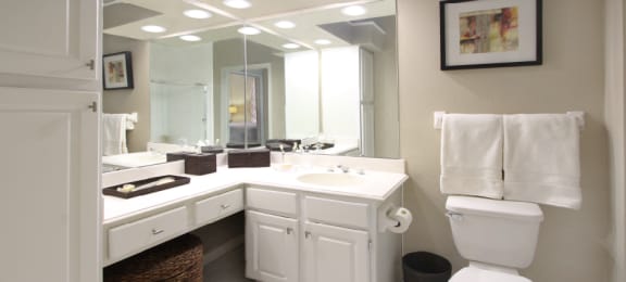 Luxury apartments with white cabinets, linen closet, extra cabinet space, cultured marble vanity, built-in vanity, and porcelain tiled floor at The Biltmore Apartments in Omaha, Nebraska