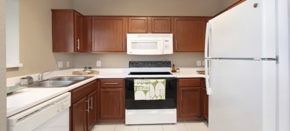 Spacious u-shaped kitchen with lots of cabinet space, lots of counter space, porcelain tile floor, and rich brown toned cabinets at The Biltmore Apartments in Omaha, Nebraska
