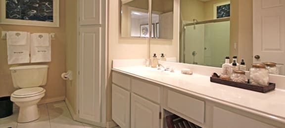 Luxury apartments with white cabinets, linen closet, extra cabinet space, cultured marble vanity, built-in vanity, roman tub with glass door and shower, and porcelain tiled floor at The Biltmore Apartments in Omaha, Nebraska